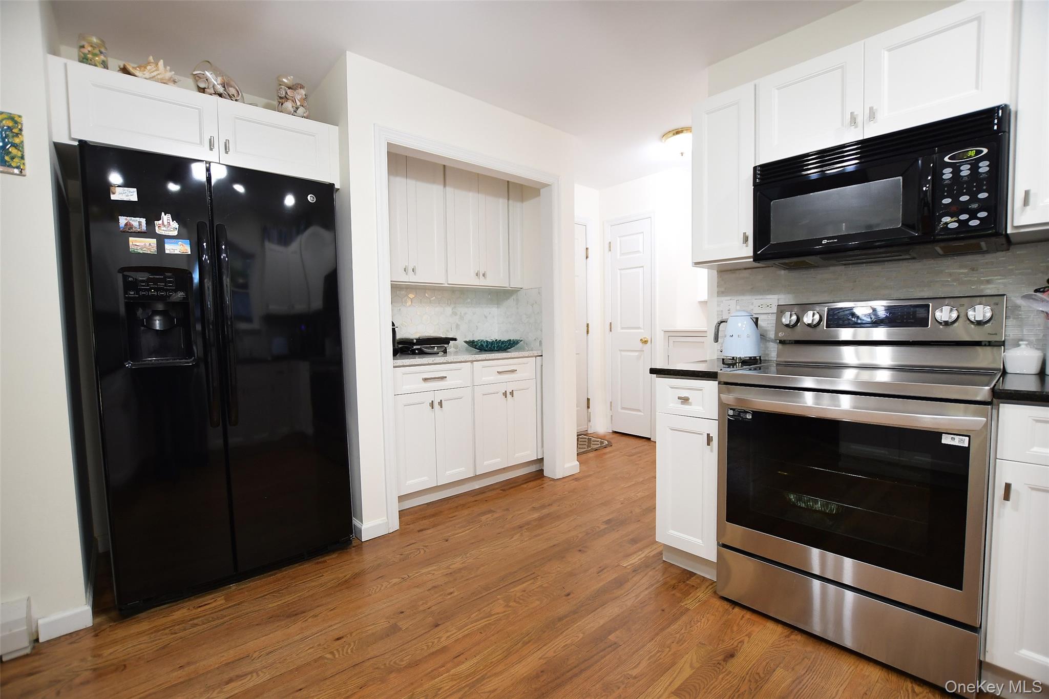 64 Glen Road Baiting Hollow, NY 11933 - Photo 10 of 46 Kitchen with black appliances, decorative backsplash, light wood finished floors, white cabinets, and dark countertops