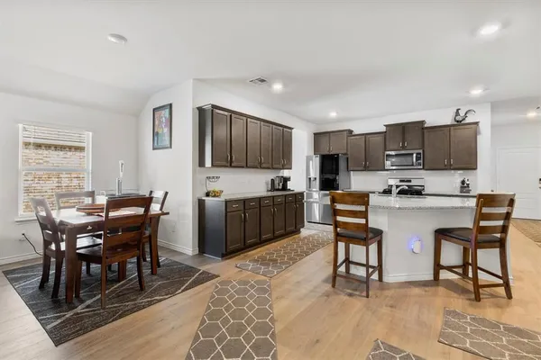 a living room with stainless steel appliances kitchen island granite countertop a dining table chairs and a refrigerator