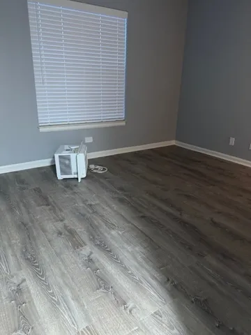 a view of an empty room with wooden floor and a window