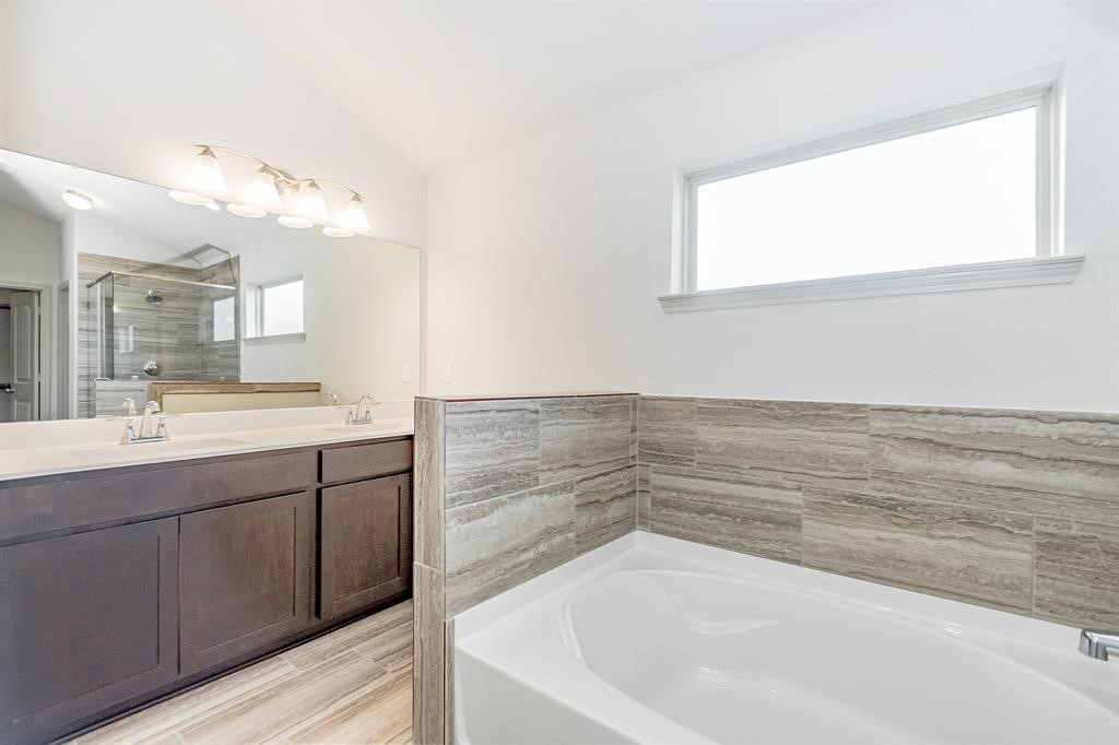 6447 Escondido Drive Rosharon, TX 77583 - Photo 10 of 16 Indulge in the spa-like ambiance of this exquisite primary bathroom. Featuring dual vanities, a deep soaking tub with tile surround, and a glass-enclosed walk-in shower, this bathroom offers both style and convenience. The large mirror and modern lighting complete the sophisticated look.