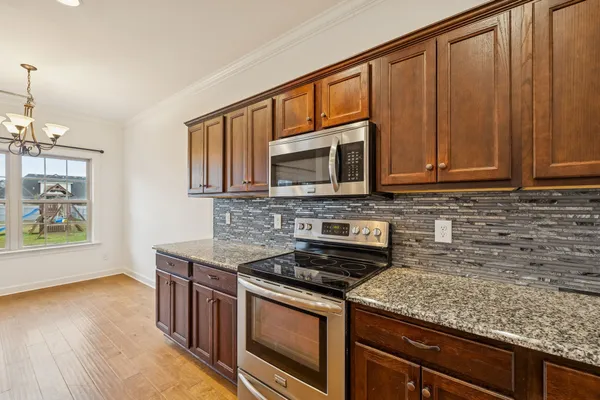 a kitchen with stainless steel appliances granite countertop a stove a microwave and wooden cabinets
