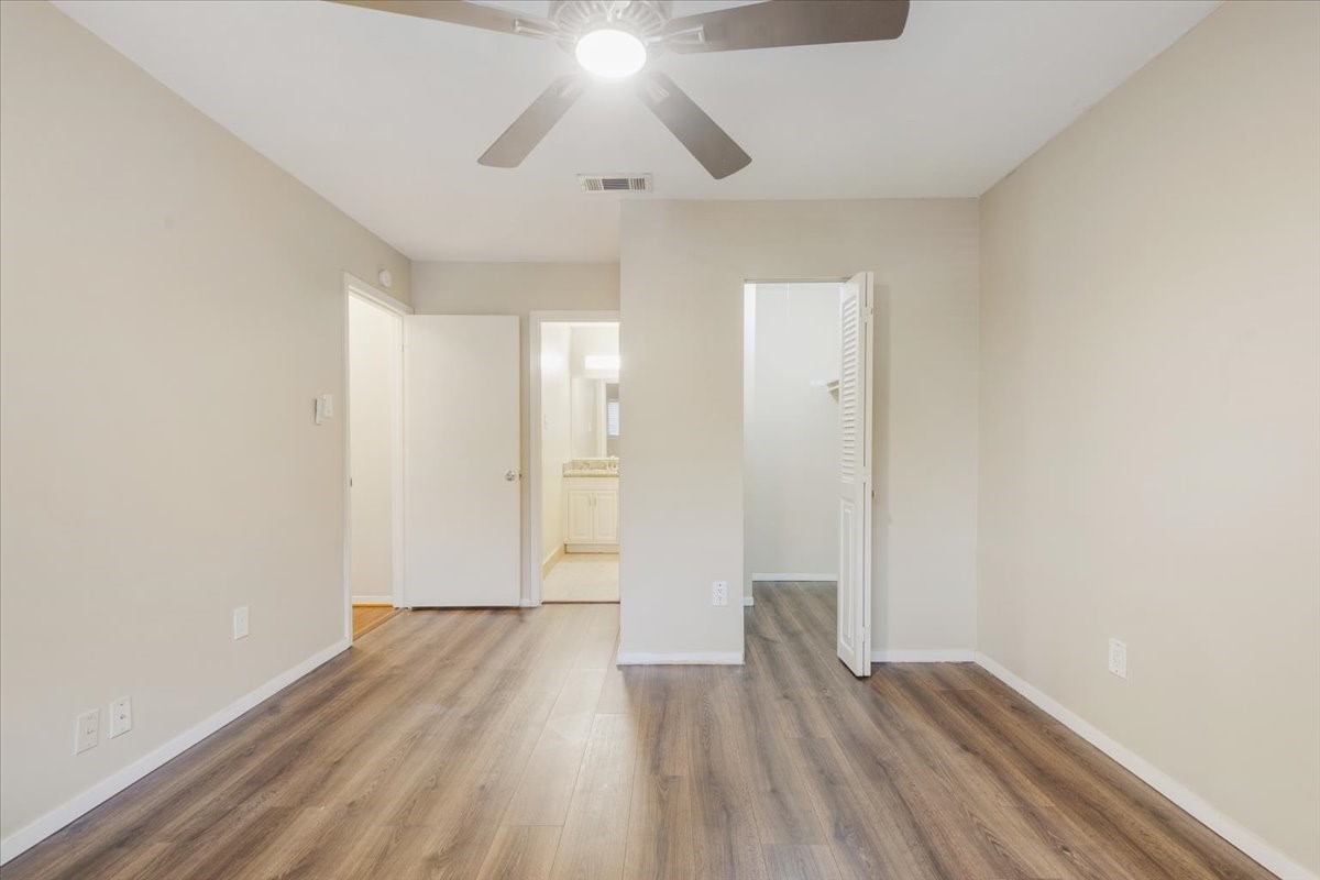 3502 Ocee Street, Unit 3502 Houston, TX 77063 - Photo 10 of 28 This photo shows a bright, neutral-toned bedroom with wood-style flooring, a ceiling fan, and a view into an adjoining bathroom and closet. It's a clean, modern space with ample natural light.