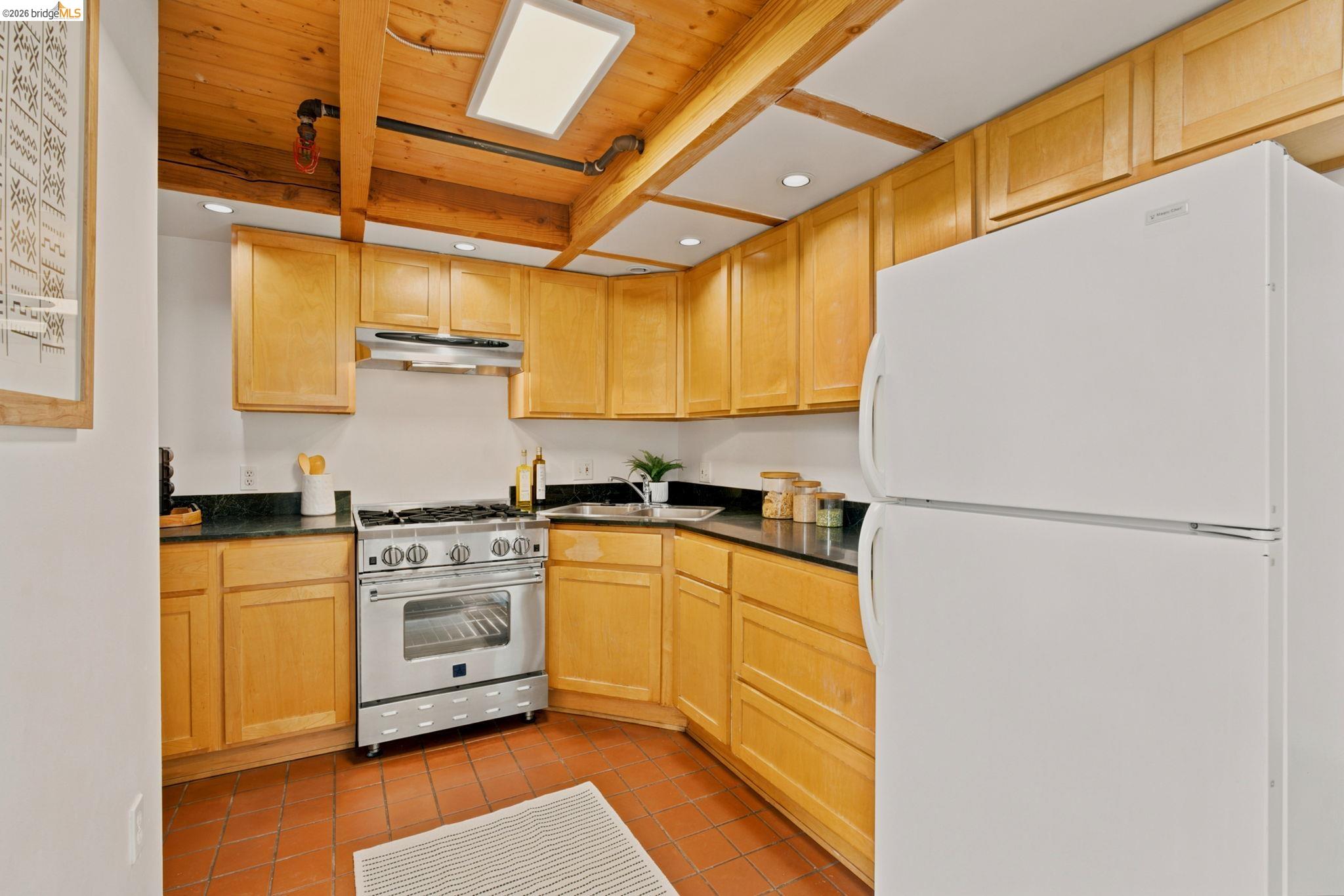 1920 Union Street, Unit 9 Oakland, CA 94607 - Photo 15 of 35 Kitchen featuring wood cabinetry, dark countertops, a stainless steel gas range with a matching range hood, and exposed wood ceiling beams