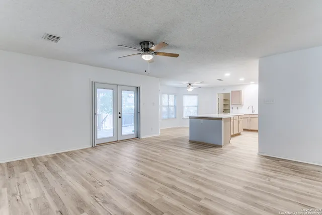 a view of an empty room and kitchen with wooden floor