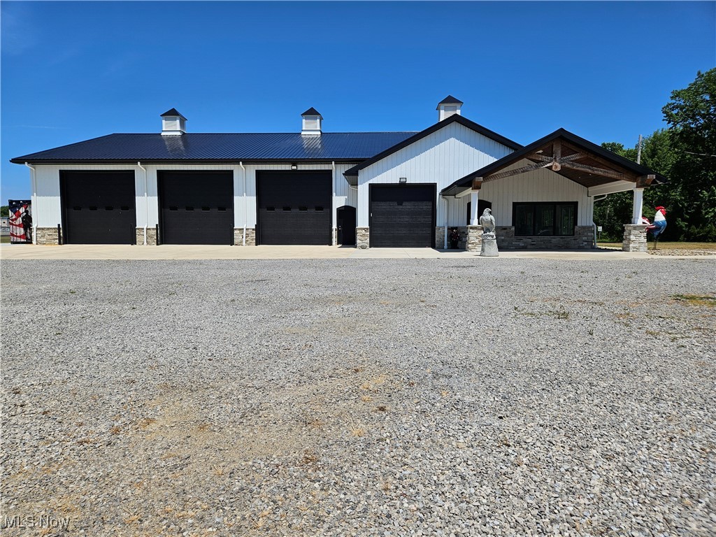 1180 North County Line Road Geneva, OH 44041 - Photo 5 of 33 View of side of property featuring board and batten siding, gravel driveway, stone siding, a metal roof, and a garage