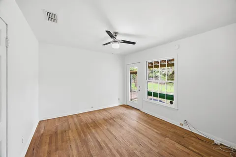 an empty room with wooden floor ceiling fan and windows