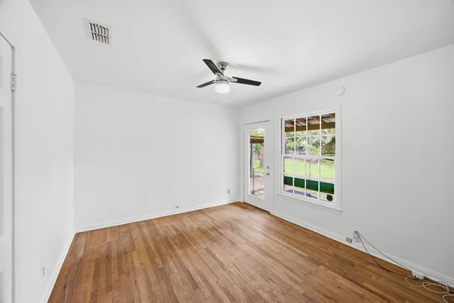 an empty room with wooden floor ceiling fan and windows