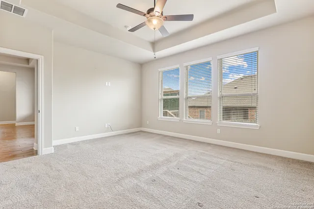 an empty room with chandelier fan and windows