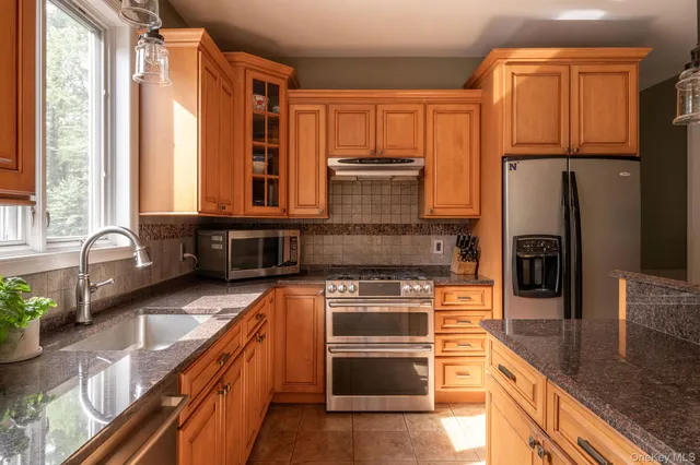 a kitchen with stainless steel appliances granite countertop a refrigerator a stove and a sink with wooden floors
