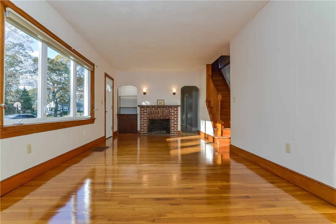 102 Davidson Road Warwick, RI 02886 - Photo 9 of 37 Living room with wood burning fireplace, built-in shelving, and arched doorway leading to kitchen. The exterior door on the left leads to a small porch, perfect for your grill.