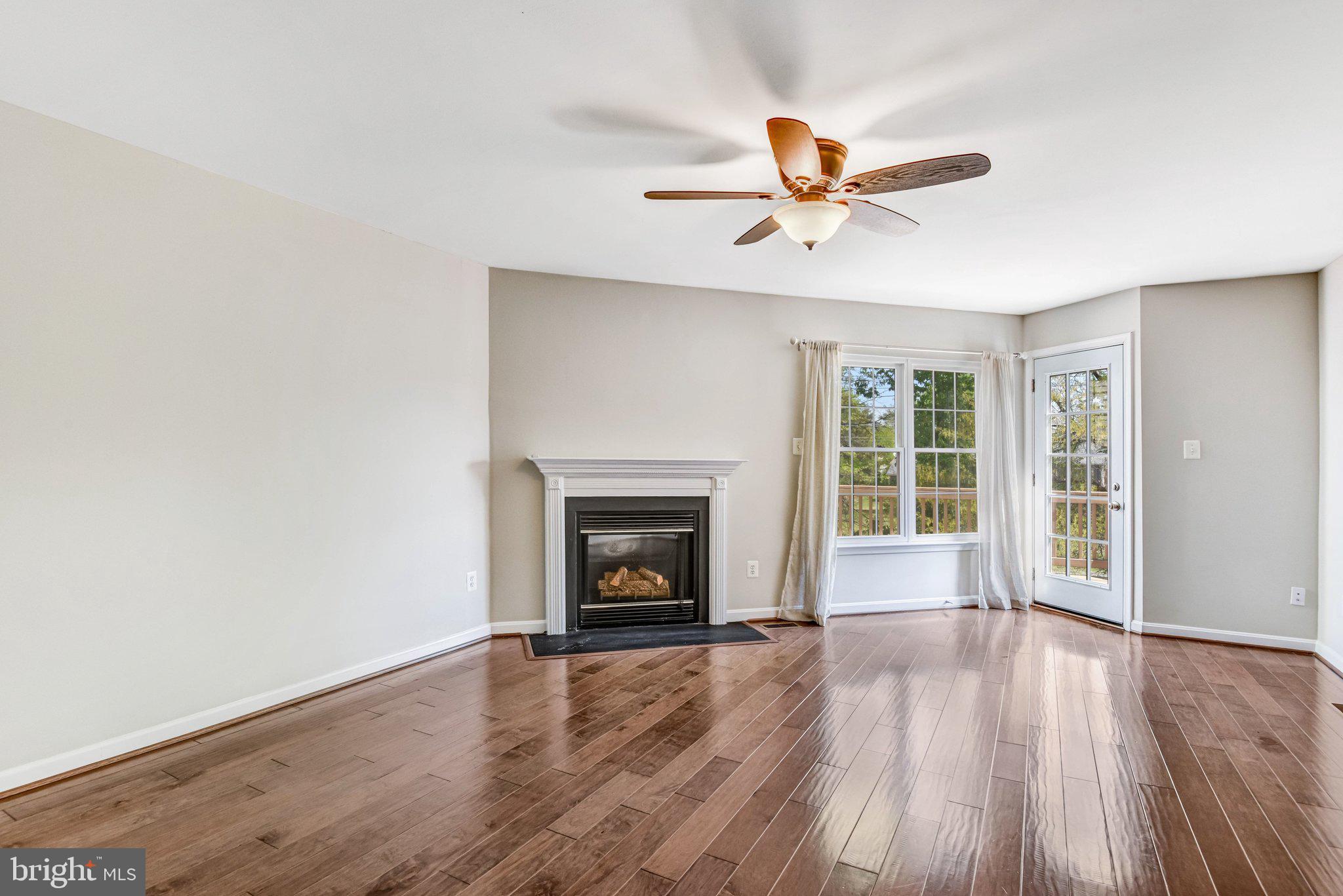 22142 Trailside Square Sterling, VA 20164 - Photo 13 of 32 an empty room with wooden floor a ceiling fan a fireplace and windows