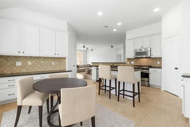 a kitchen with stainless steel appliances granite countertop a table chairs sink and cabinets