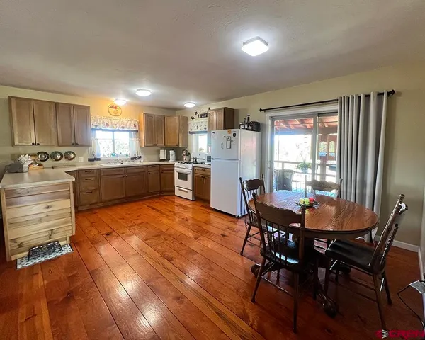 a kitchen with stainless steel appliances granite countertop a stove a refrigerator a kitchen island a dining table and chairs with wooden floor