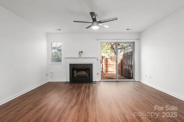a view of an empty room with wooden floor fireplace and a window