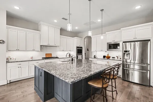 a large kitchen with granite countertop a stove a sink dishwasher a refrigerator with white cabinets and couches