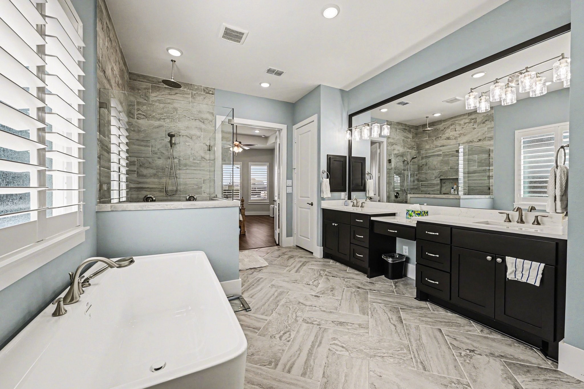 2311 Legends Way Katy, TX 77493 - Photo 30 of 50 Spa-inspired primary bath designed for relaxation, featuring a freestanding soaking tub, oversized walk-in shower with floor-to-ceiling tile, and stunning herringbone-patterned flooring. Dual vanities with quartz countertops and designer lighting complete this luxurious retreat.