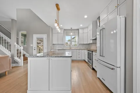 a kitchen with stainless steel appliances granite countertop a refrigerator a sink dishwasher a stove and white countertops with wooden floor
