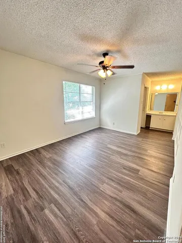 an empty room with wooden floor chandelier fan and windows