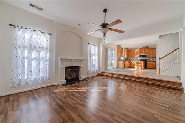 a view of a livingroom with wooden floor a fireplace a ceiling fan and window