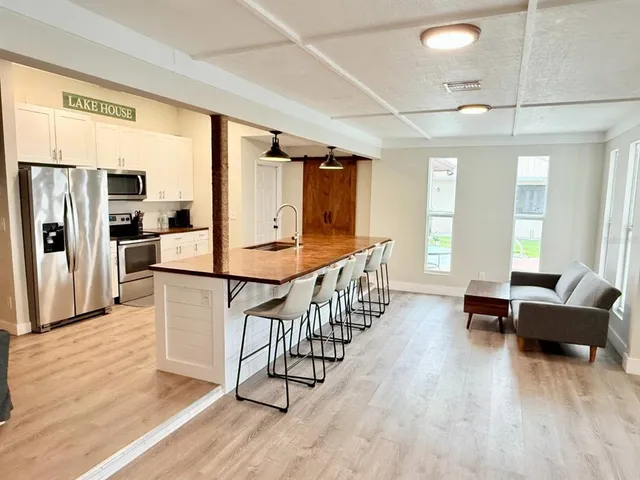 a kitchen with stainless steel appliances kitchen island granite countertop a refrigerator a stove a dining table and chairs with wooden floor