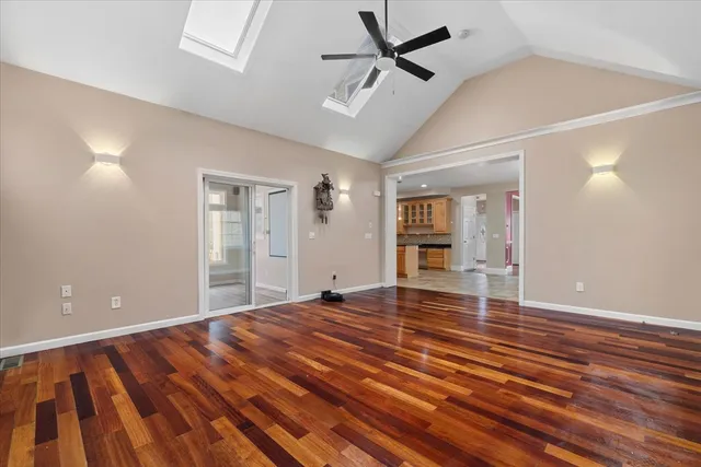 a view of an empty room with wooden floor kitchen view and a window