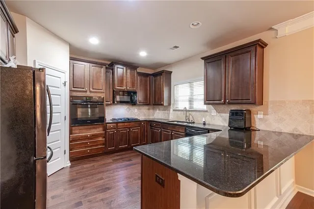 a kitchen with stainless steel appliances granite countertop wooden cabinets a sink and dishwasher a stove top oven with wooden floor