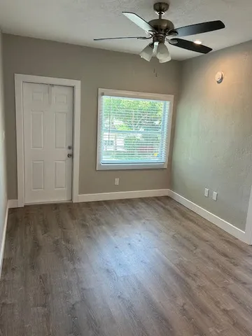 an empty room with wooden floor chandelier fan and windows