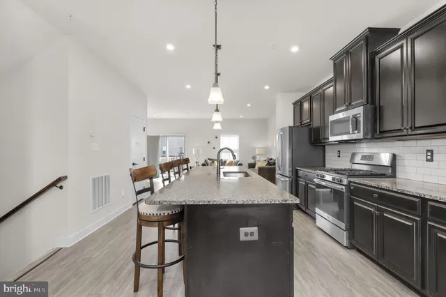 a kitchen with stainless steel appliances granite countertop a sink a stove a refrigerator and island with wooden floor