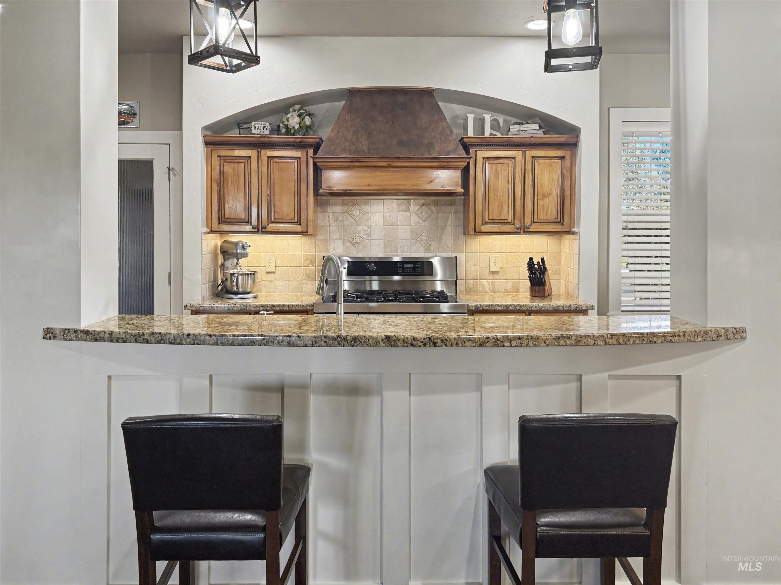 2425 South Chipper Way Eagle, ID 83616 - Photo 40 of 43 Kitchen featuring brown cabinets, custom range hood, a breakfast bar area, and stainless steel range with gas stovetop