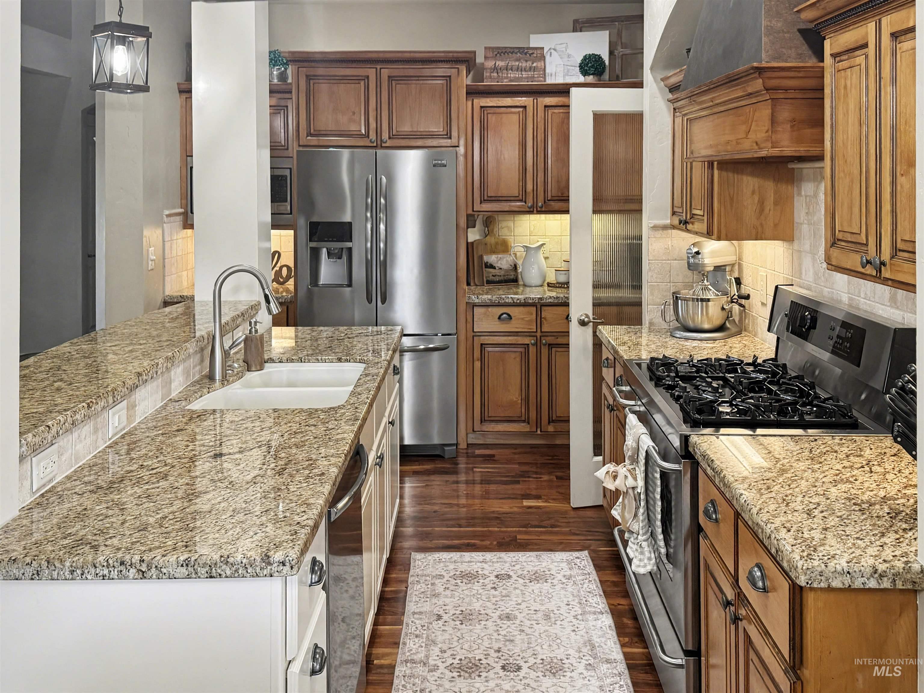 2425 South Chipper Way Eagle, ID 83616 - Photo 9 of 43 Kitchen with appliances with stainless steel finishes, brown cabinets, light stone counters, tasteful backsplash, and hanging light fixtures
