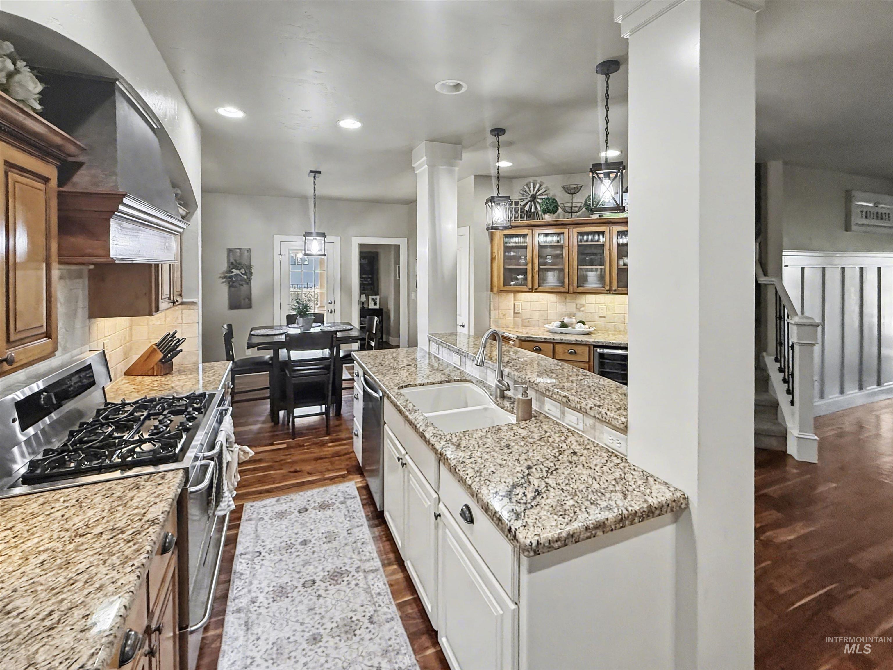 2425 South Chipper Way Eagle, ID 83616 - Photo 10 of 43 Kitchen featuring stainless steel appliances, decorative light fixtures, glass insert cabinets, light stone countertops, and dark wood-style flooring