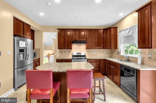 a kitchen with stainless steel appliances granite countertop a table chairs sink refrigerator and cabinets