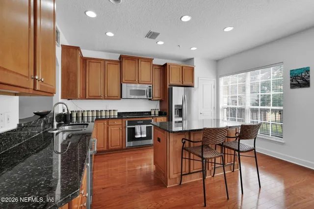 a kitchen with stainless steel appliances granite countertop a stove top oven a sink dishwasher a dining table and chairs with wooden floor