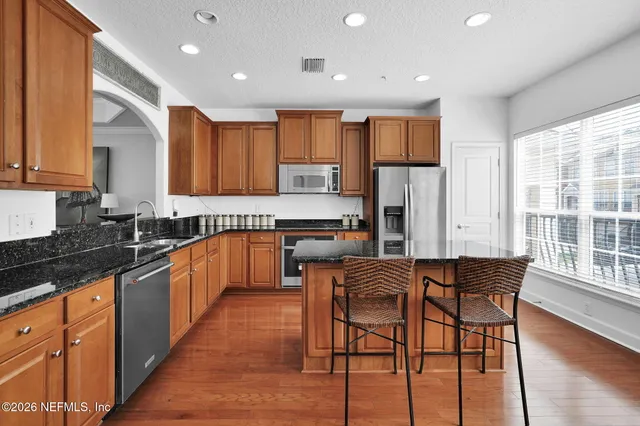 a kitchen with stainless steel appliances granite countertop wooden cabinets a sink a stove a dining table and chairs