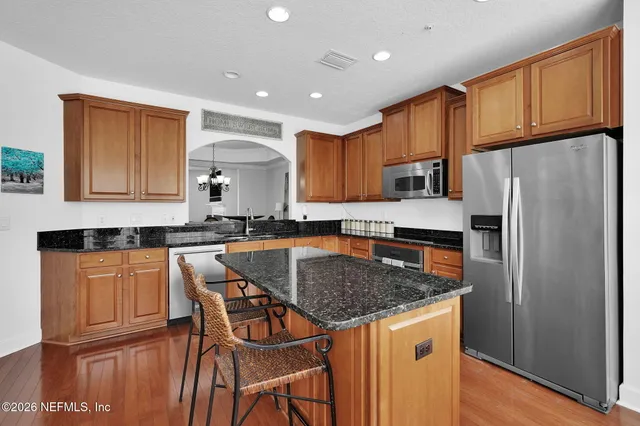 a kitchen with stainless steel appliances granite countertop a refrigerator a sink dishwasher a stove with wooden cabinets and floor