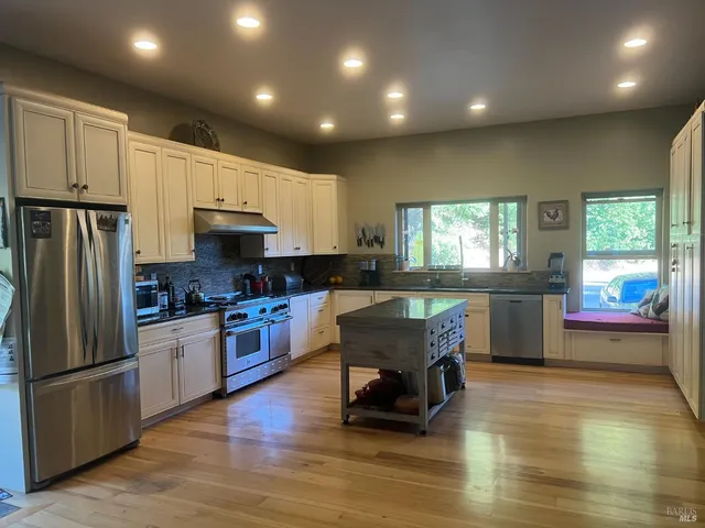 a kitchen with stainless steel appliances granite countertop a refrigerator a stove top oven a sink dishwasher and white cabinets with wooden floor