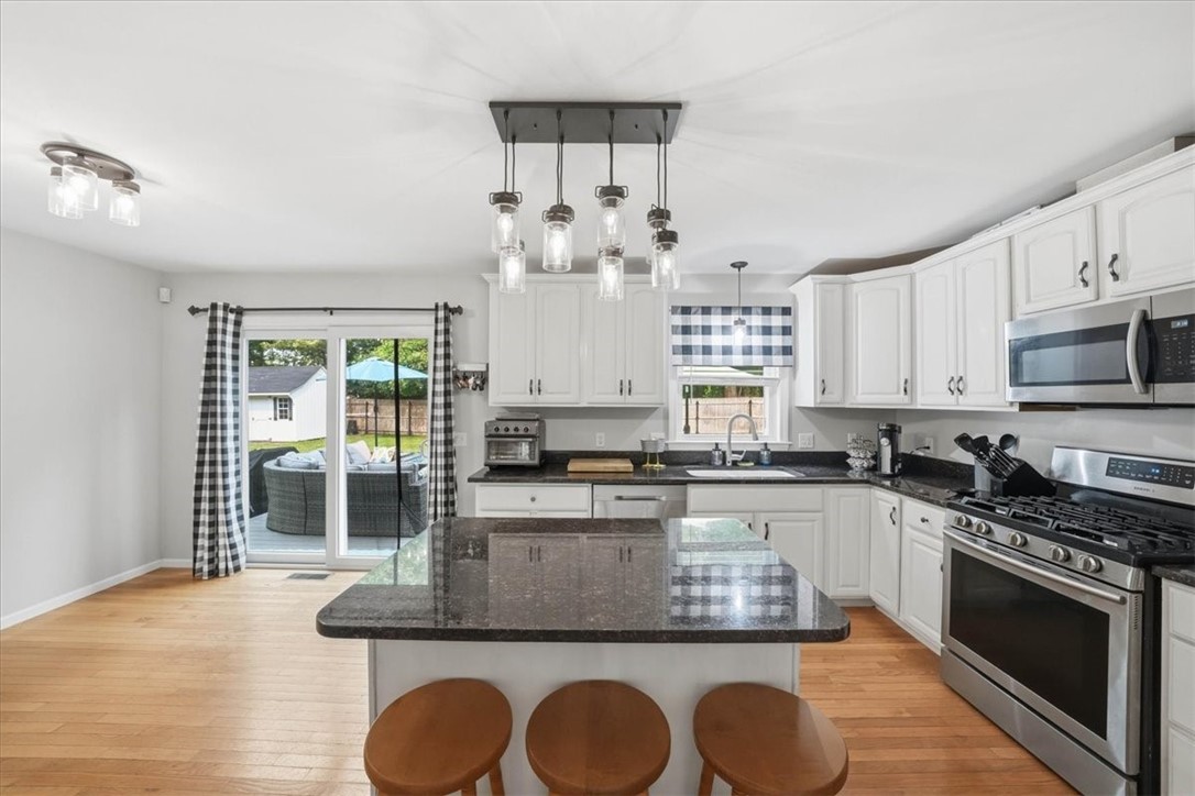 26 Davis Circle Warwick, RI 02886 - Photo 17 of 50 White raised-panel cabinetry is complemented by granite countertops, stainless steel appliances, hardwood flooring, and a large center island perfect for meal prep, casual dining, or entertaining guests.