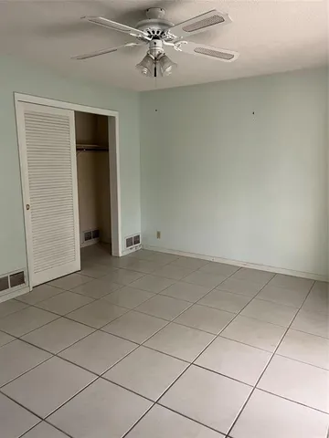 an empty room with chandelier fan and kitchen space