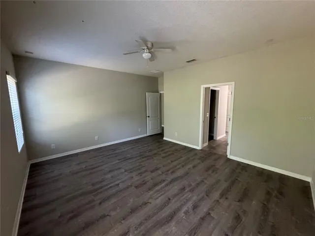 an empty room with wooden floor chandelier fan and windows
