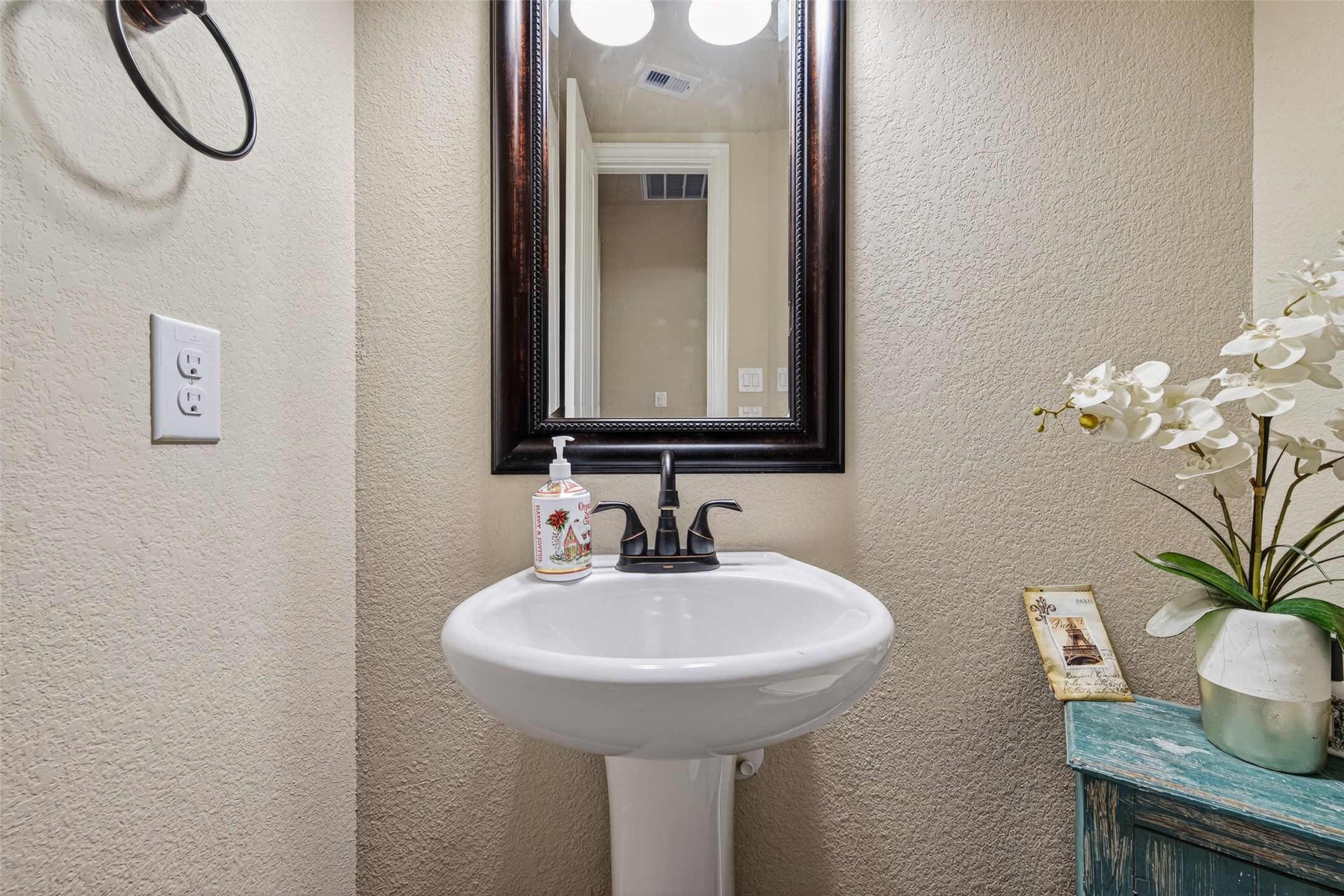 25611 Ellis Ridge Court Katy, TX 77494 - Photo 20 of 49 This is a compact, stylish half-bathroom featuring a pedestal sink, a decorative mirror, and a small countertop with a vase of flowers for a touch of elegance.