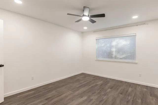 an empty room with wooden floor ceiling fan and windows