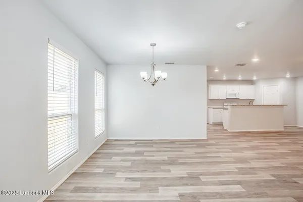 an empty room with wooden floor kitchen view and windows