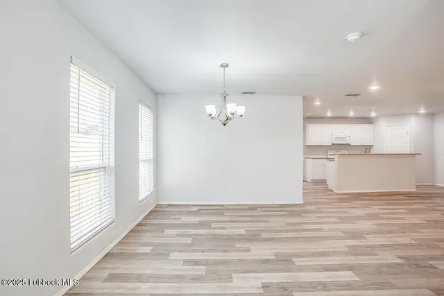 an empty room with wooden floor kitchen view and windows