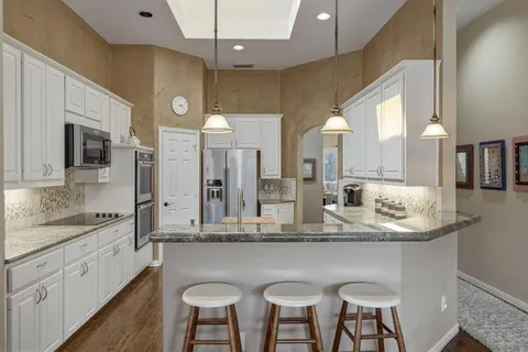a kitchen with stainless steel appliances kitchen island granite countertop a table chairs sink and cabinets