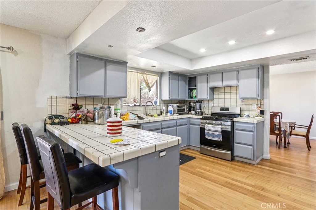 14057 Crow Road Apple Valley, CA 92307 - Photo 14 of 33 a kitchen with a stove a sink a kitchen island with chairs and wooden cabinets