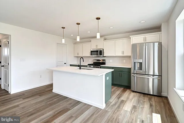 a kitchen with stainless steel appliances granite countertop a refrigerator a stove a sink and white cabinets with wooden floor