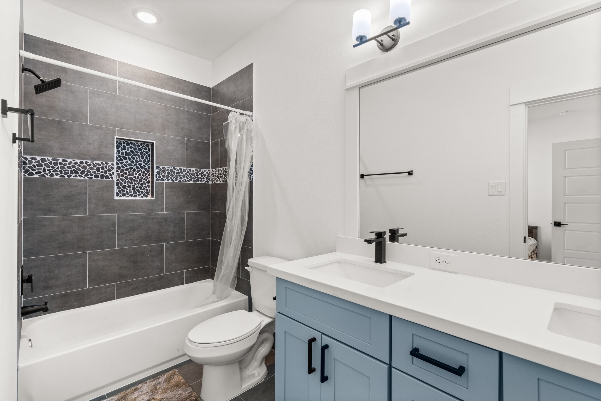 2928 Stevens Street Houston, TX 77026 - Photo 16 of 30 This modern bathroom features a sleek design with a double vanity in blue cabinetry, stylish black fixtures, and a large mirror. The bathtub-shower combo is accented by dark gray tiles with a decorative mosaic strip, creating a contemporary, inviting space.