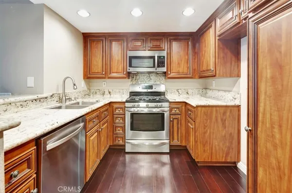 a kitchen with granite countertop wooden floors white cabinets and stainless steel appliances