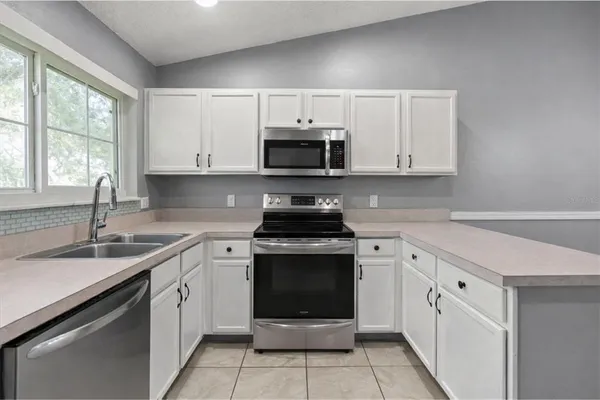 a kitchen with white cabinets appliances a sink and a window