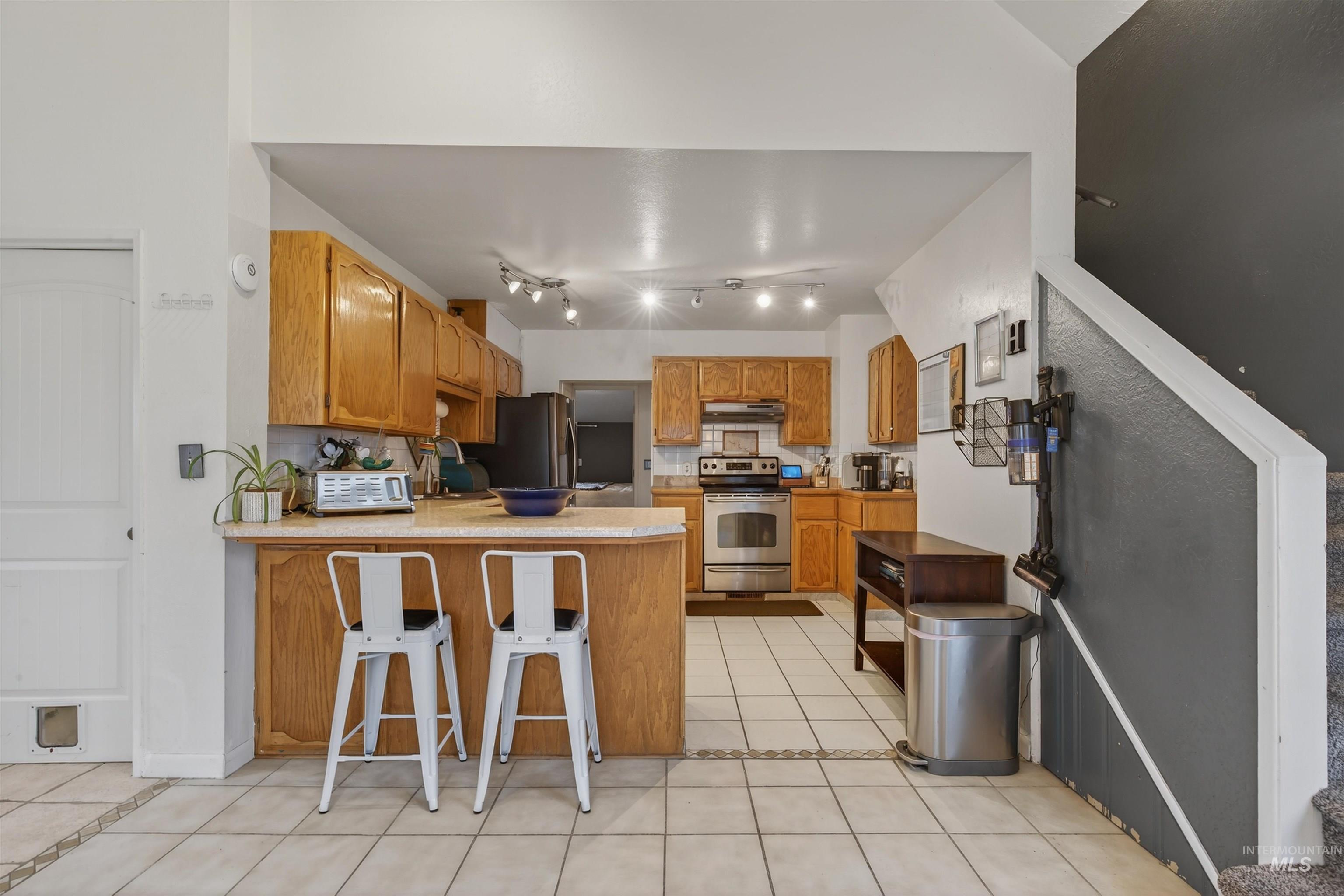 1266 Poplar Street Clarkston, WA 99403 - Photo 10 of 31 Kitchen featuring light tile patterned flooring, wood finish cabinetry, a peninsula, stainless steel appliances, and a breakfast bar area